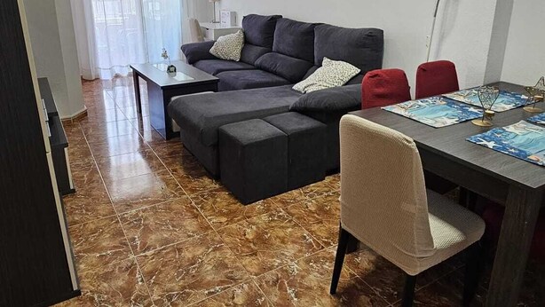 A living room with a sofa, a dining table with placemats, a chair, and a clock on the wall. - Fantastic 4-bedroom apartment, only 150m from the beach of Los Locos, Torrevieja (Torrevieja)