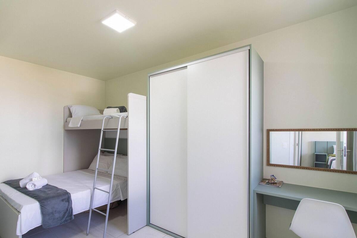 Ein kleines Zimmer mit Etagenbett, Schreibtisch und Stuhl sowie einem großen Spiegel.