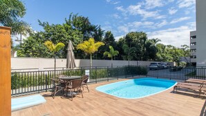 Een zwembad met ligbedden, een tafel met stoelen en een pergola met een parasol.