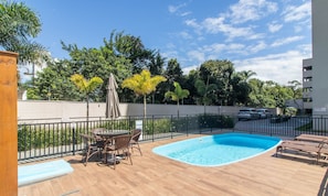 Ein Schwimmbecken mit Liegestühlen, einem Tisch mit Stühlen und einer Pergola mit Sonnenschirm.