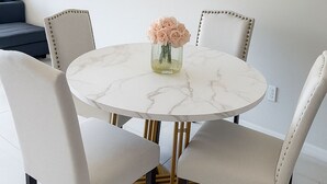 A round dining table with four chairs, a vase with flowers, and a framed picture on the wall. - Spacious 3-Bedroom Getaway — Perfect for Families or Groups!” (Cape Coral)