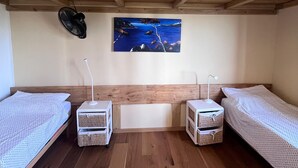 Habitación con dos camas individuales, piso de madera, ventilador de techo, un cuadro y dos mesitas de noche con cestas.