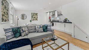 Een moderne woonkamer met een grijze bank, decoratieve kussens, een salontafel en een keuken op de achtergrond.