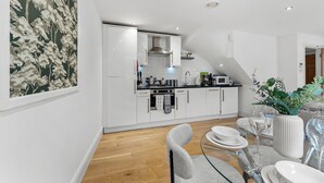 Een moderne keuken met witte kasten, een zwart aanrecht en een eethoek met een glazen tafel en stoelen.