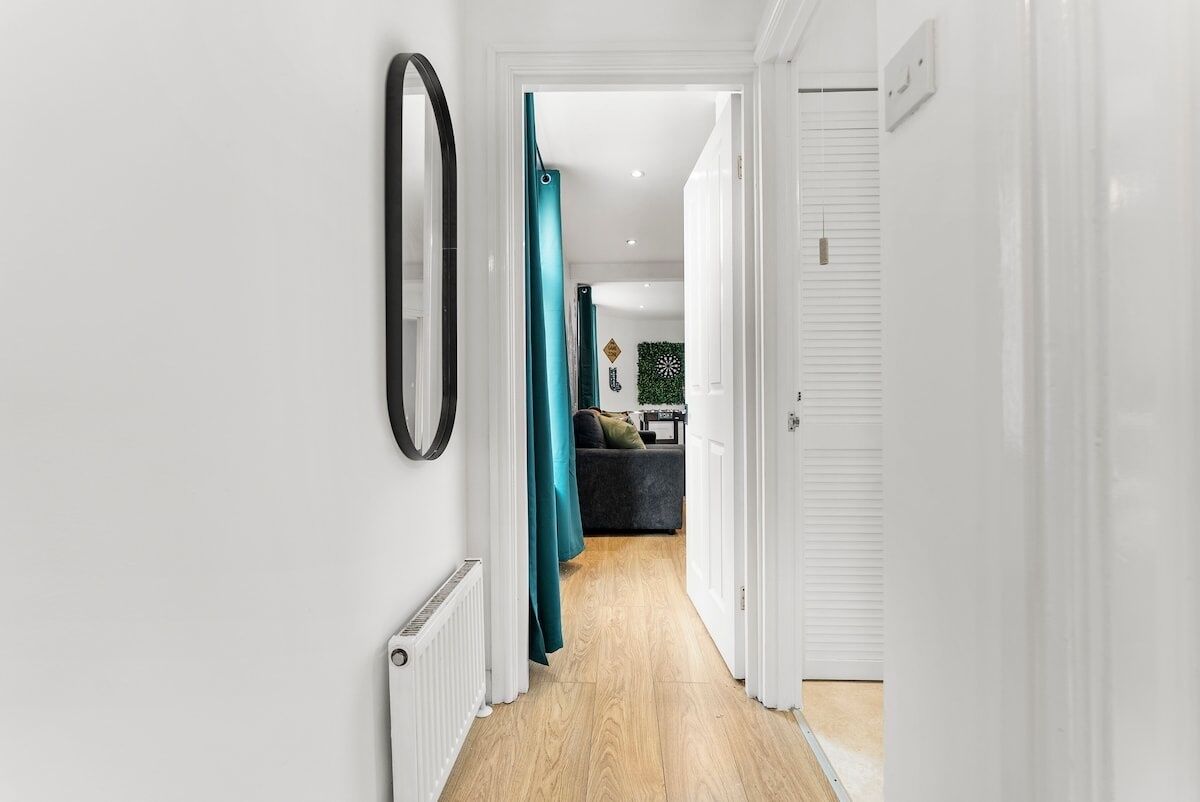 Un couloir avec un radiateur, un rideau de couleur turquoise et une porte donnant sur une pièce où se trouve un canapé de couleur sombre et un élément décoratif mural.