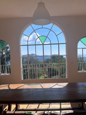 Une pièce dotée d’une grande fenêtre en arc de cercle, d’une table en bois et offrant une vue sur un paysage montagneux.