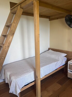 A single bed with a patterned bedspread in a room with wooden beams and a ceiling fan.