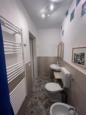 A small bathroom with a toilet, bidet, sink, and a radiator.