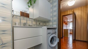 A modern laundry room with a washing machine, a drying rack, and a cabinet.