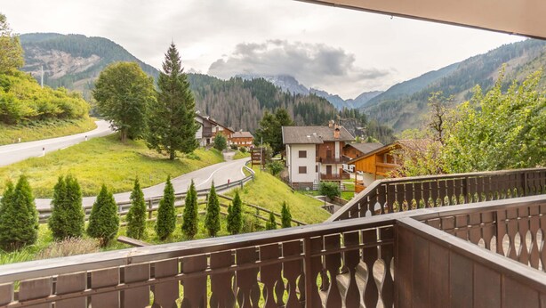 A view from a balcony overlooking a mountainous landscape with houses and a winding road.