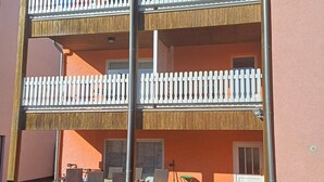 Un immeuble à plusieurs étages, avec une clôture blanche en bois, des sièges à l’extérieur et un vélo.