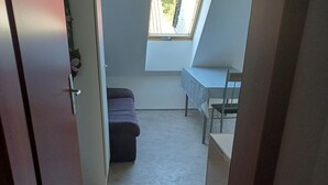 Un couloir étroit mène à une pièce dont le plafond est incliné, qui possède une petite fenêtre et une table entourée de chaises.