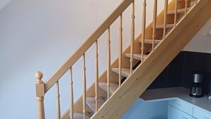 Un escalier en bois, une poubelle bleue et un coin cuisine avec une machine à café.