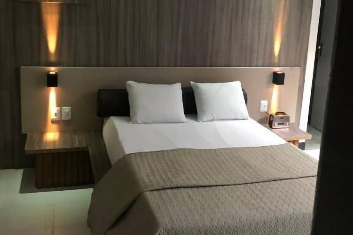 A modern hotel room with a large bed, wooden headboard, and two bedside tables with lamps.
