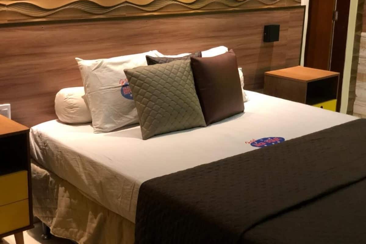 A neatly made bed with a quilted pillow, a brown pillow, and a pillow with a logo.