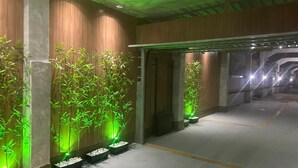 A corridor with green-lit bamboo plants and a concrete floor.
