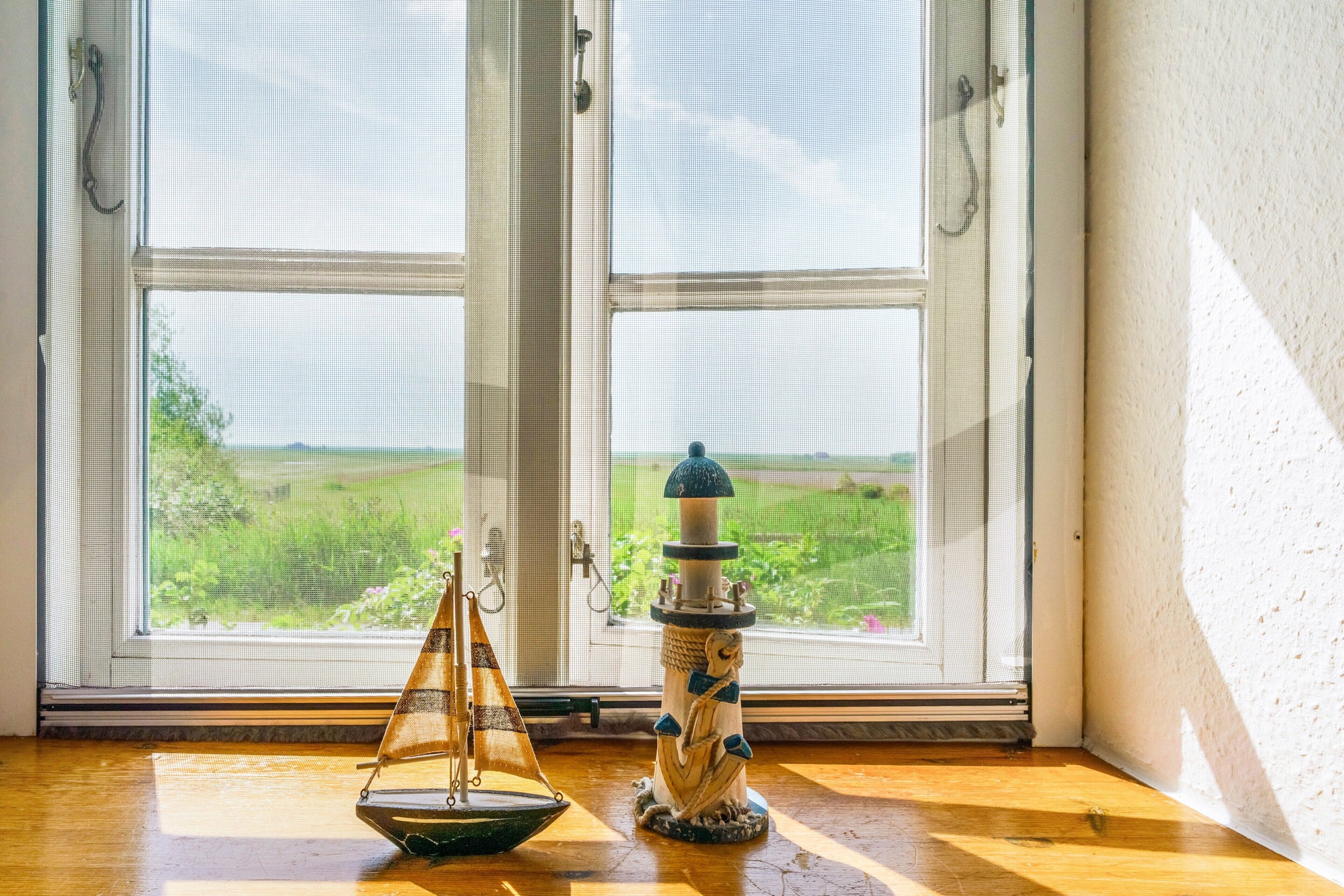 Ein Zimmer mit Holzboden, einem Fenster mit Blick auf ein grünes Feld und einem dekorativen Gegenstand in der Fensterbank.