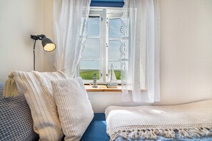 Une chambre avec un lit, une fenêtre donnant sur un beau paysage, une lampe et une petite table sur laquelle sont posés quelques objets.