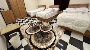 A hotel room with two single beds and one double bed, a checkered floor, a wooden wardrobe, a small table with a lamp, and a decorative rug. - Great Pyramids Lodge (Giza)