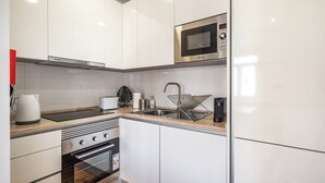 Ett modernt kök med vita skåp, en mikrovågsugn i rostfritt stål, en inbyggd ugn, en diskho och en vattenkokare.