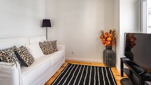 Ett modernt vardagsrum med en vit soffa, en svartvit randig matta, en svart lampa och en vas med orange blommor.
