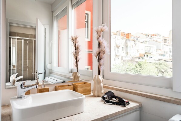 Une salle de bain moderne avec un grand lavabo blanc, un miroir et deux vases contenant des plantes séchées.