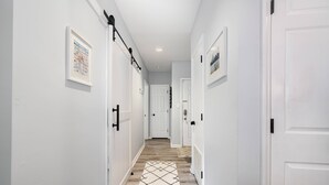 A hallway with white walls, a patterned rug, and a wooden floor.