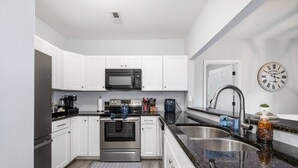 A modern kitchen with white cabinets, stainless steel appliances, a black granite countertop, and a wall clock.
