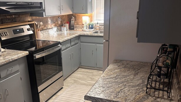 A kitchen with grey cabinets, a stainless steel stove, a refrigerator, and a granite countertop. - Charming 3-bedroom house with AC in nice Hope Hull. (hope hull)