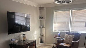A living room with a flat-screen TV, a coffee table, a brown leather sofa, a patterned rug, and a ceiling fan. - Charming 3-bedroom house with AC in nice Hope Hull. (hope hull)