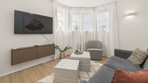 Un salon moderne avec un canapé gris, un meuble en bois, une table basse et un téléviseur fixé au mur.