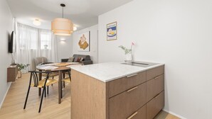 Une cuisine moderne dotée d’un îlot central, un coin repas avec une table ronde et un espace de vie comprenant un canapé et un téléviseur.