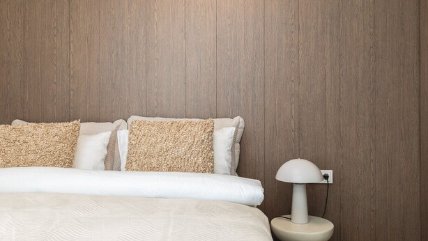 Une chambre avec un mur en bois, un lit avec une literie blanche et une lampe de chevet.
