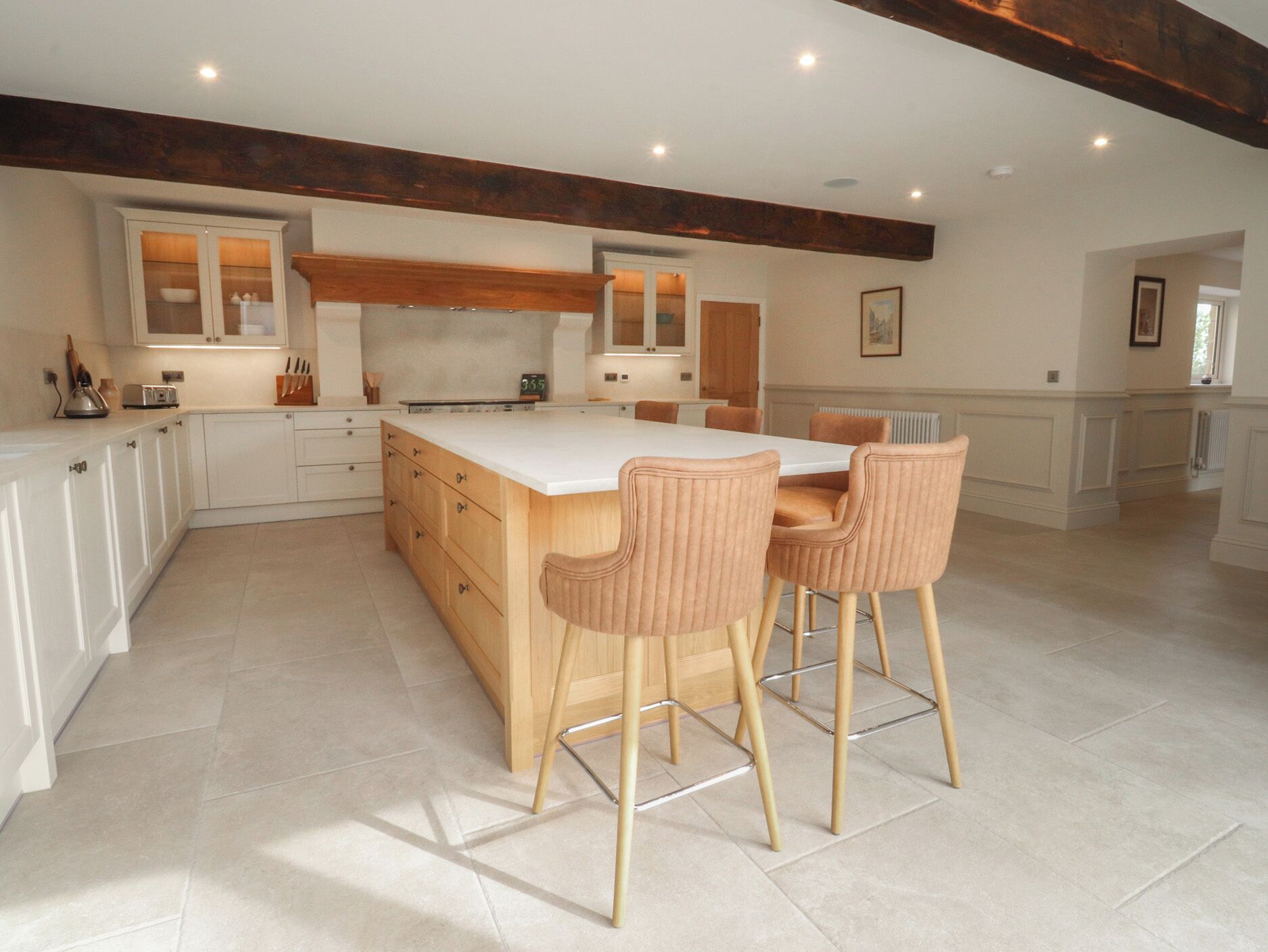 A modern kitchen with a central island, white cabinetry, and a wooden ceiling beam.