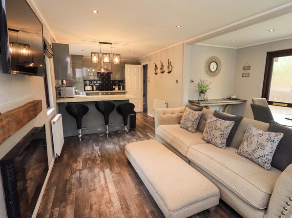A modern kitchen with bar stools, a sofa with patterned cushions, and a dining area with a table and chairs.