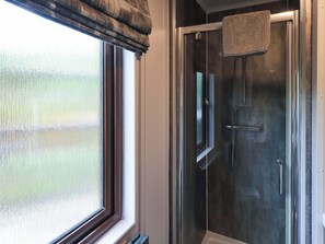 A bathroom with a glass shower enclosure, a window with blinds, and a towel hanging on a rack.