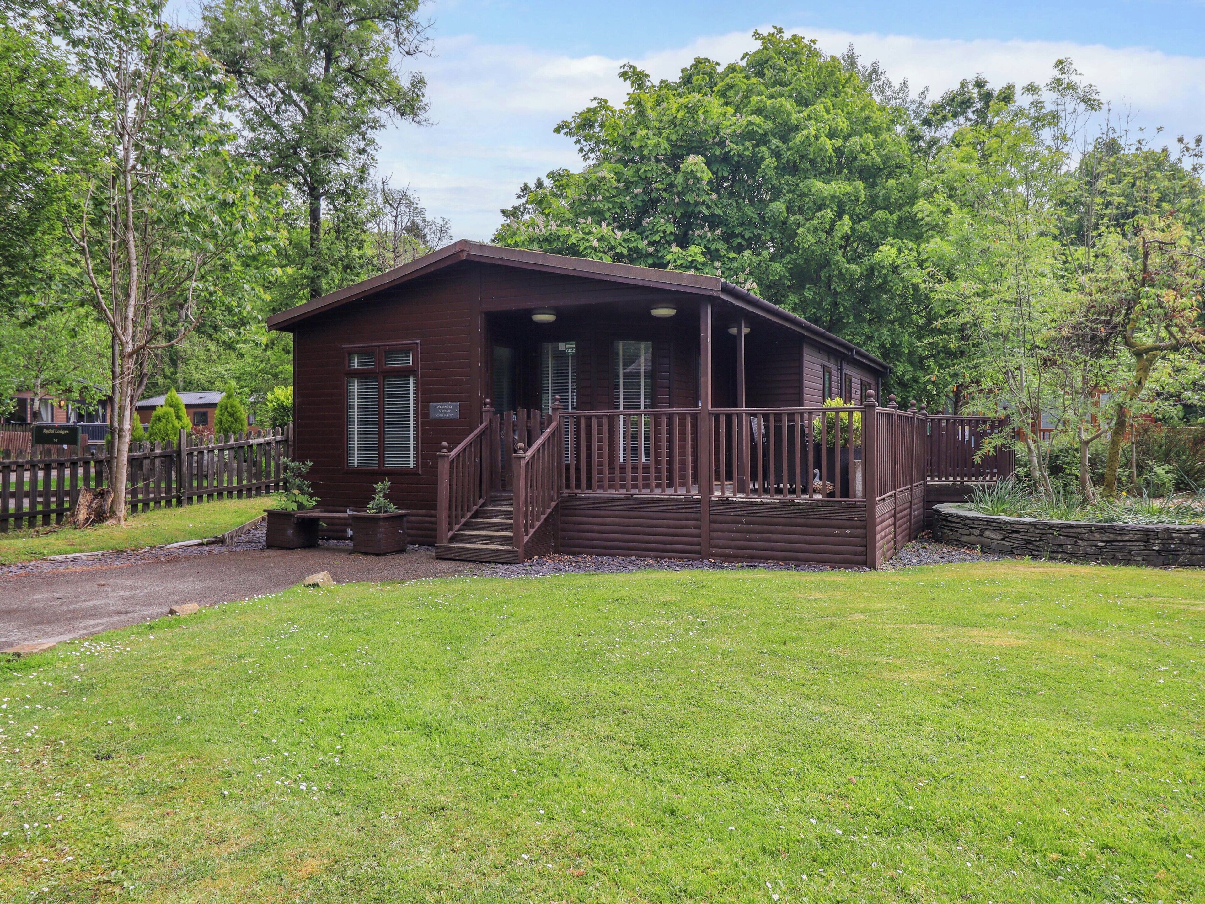A single-story wooden cabin with a porch, surrounded by a grassy yard and trees.