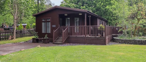 Een houten vakantiebungalow met een veranda, gelegen in een gazon met bomen.