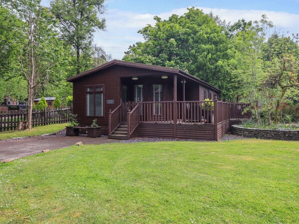 Ein eingeschossiges Holzhaus mit Veranda, umgeben von einem grasbewachsenen Garten und Bäumen.