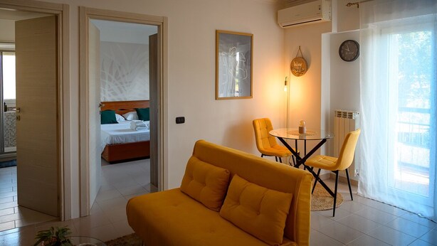 Ein modernes Hotelzimmer mit einem Bett, einer Couch, einem Esstisch mit Stühlen und einem großen Fenster mit Vorhängen.
