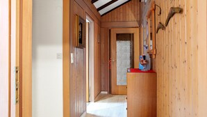 Un couloir en bois avec une porte donnant sur une pièce, un porte-manteau et une petite table sur laquelle se trouve un objet en verre.