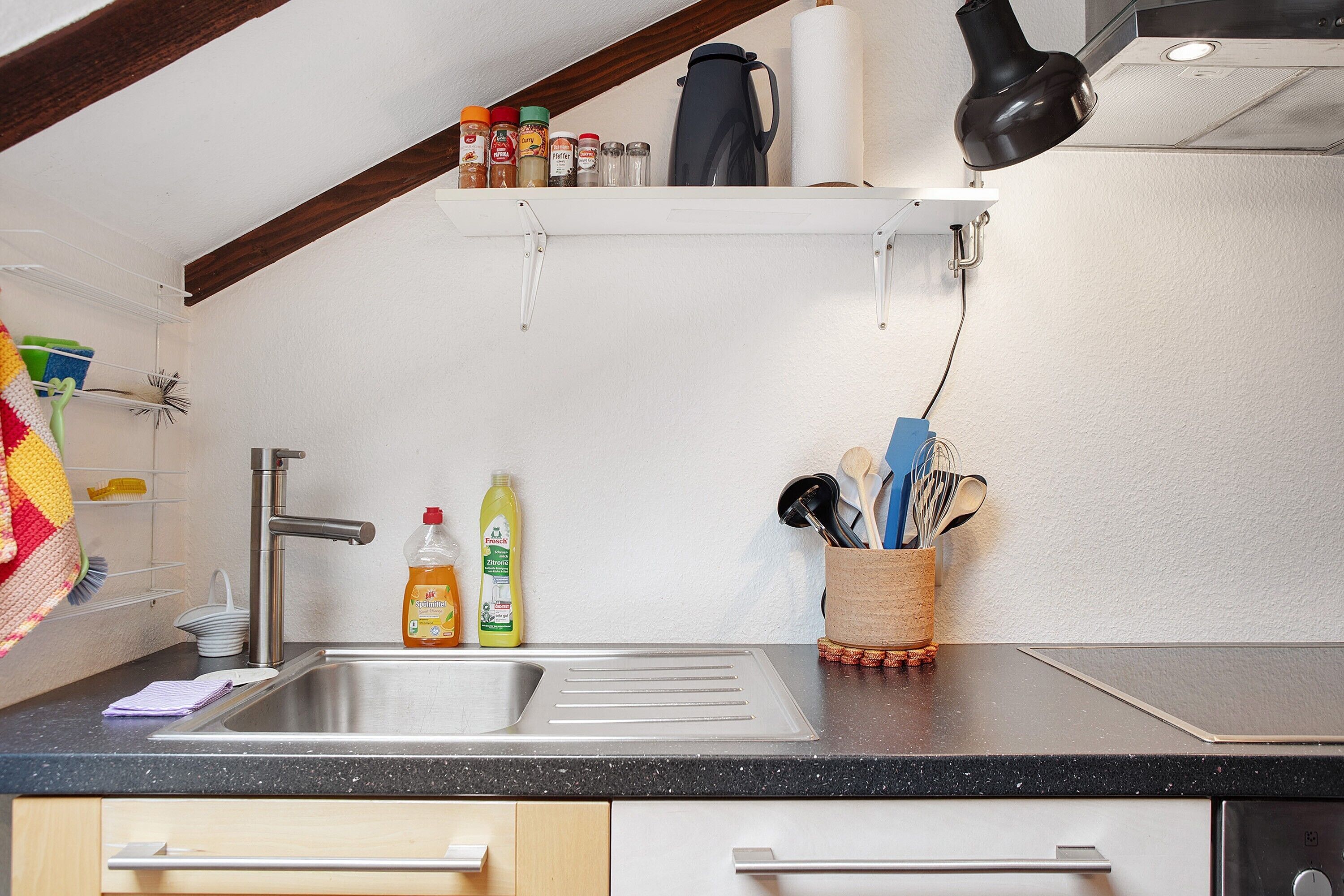 A kitchen with a stainless steel sink, a coffee maker, and a spice rack.
