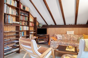 A cozy living room with wooden bookshelves, a sofa, a television, and a wooden ceiling. - Haus Palais with Covered Balcony, Mountain View, and Wi-Fi (Münstertal)