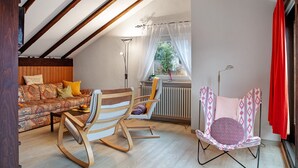 Une pièce chaleureuse avec un plafond en bois, un canapé à motifs, un fauteuil à bascule et une chaise pliante avec un coussin.