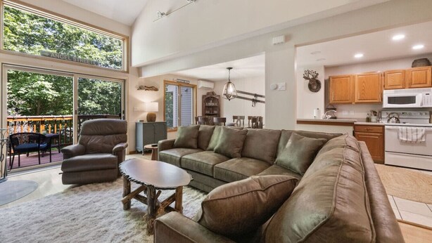 A spacious living room with a large sectional sofa, a wooden coffee table, and a dining area with a kitchen in the background.