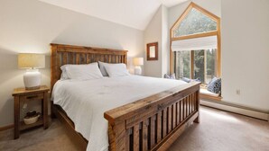 A bedroom with a wooden bed, two bedside tables, a window with a view, and a small window seat.