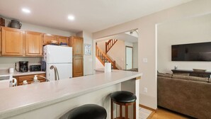 A modern kitchen with wooden cabinets, a white refrigerator, a coffee maker, and a bar stool.
