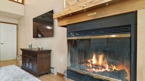 A living room with a fireplace, wooden cabinet, and a television mounted on the wall.