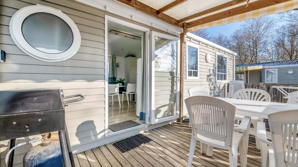 Une terrasse couverte équipée d’un barbecue, de chaises en plastique blanc et d’une porte-fenêtre coulissante donnant sur l’intérieur.
