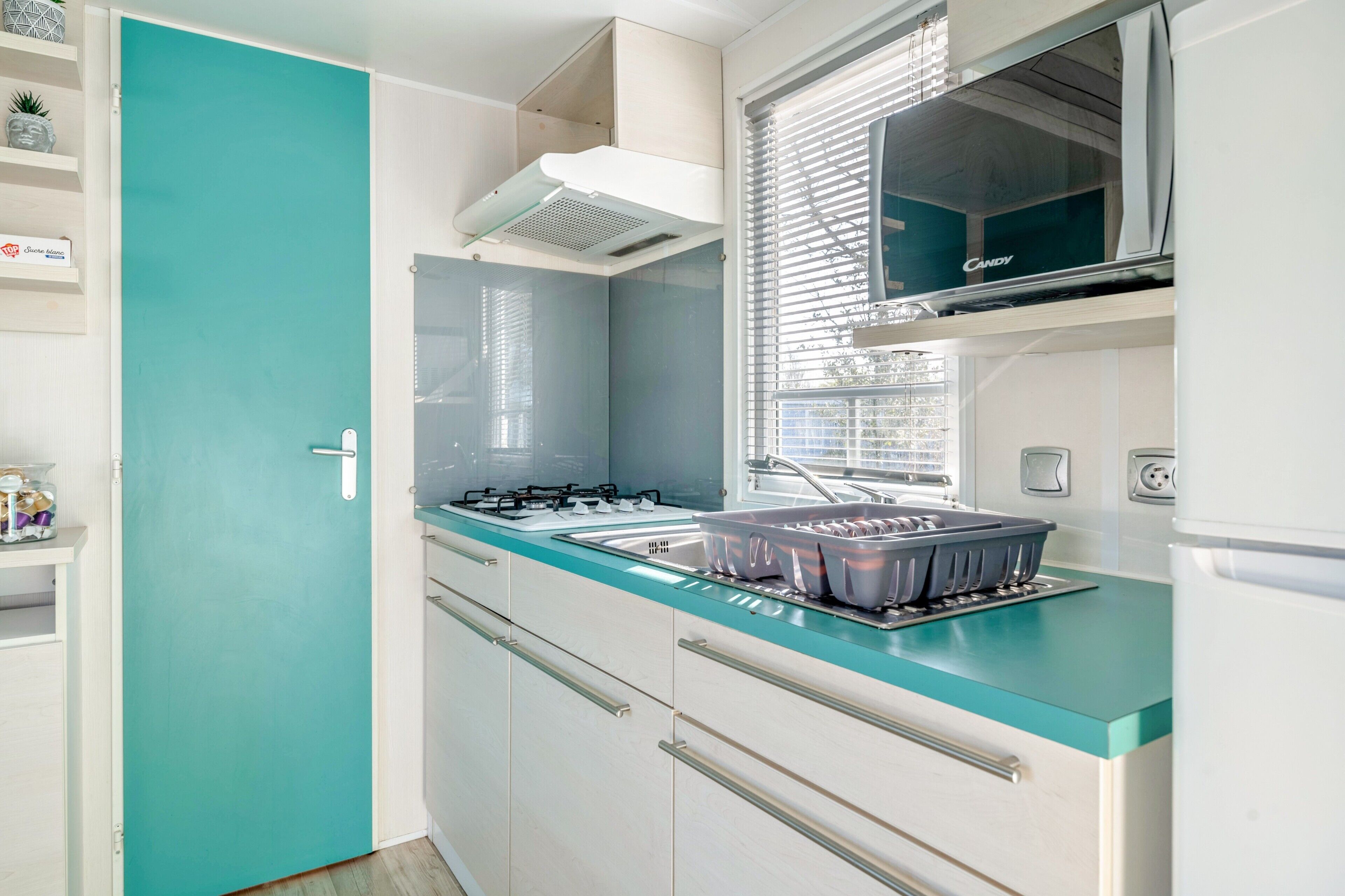A kitchen with a teal countertop, a gas stove, a sink, and a window with blinds.